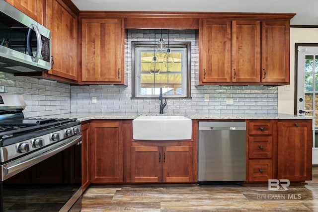 kitchen with appliances with stainless steel finishes, light stone countertops, sink, and light hardwood / wood-style floors