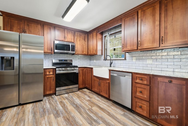 kitchen featuring light hardwood / wood-style floors, sink, decorative backsplash, light stone countertops, and appliances with stainless steel finishes