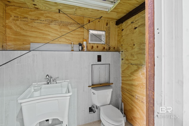 bathroom with sink, wood walls, toilet, and tile walls