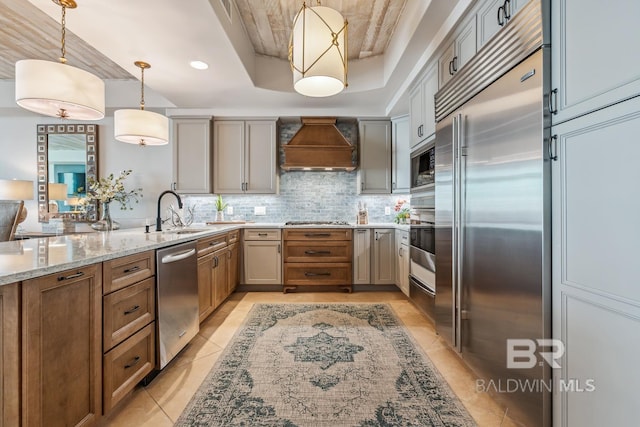 kitchen featuring a sink, a tray ceiling, tasteful backsplash, built in appliances, and custom exhaust hood