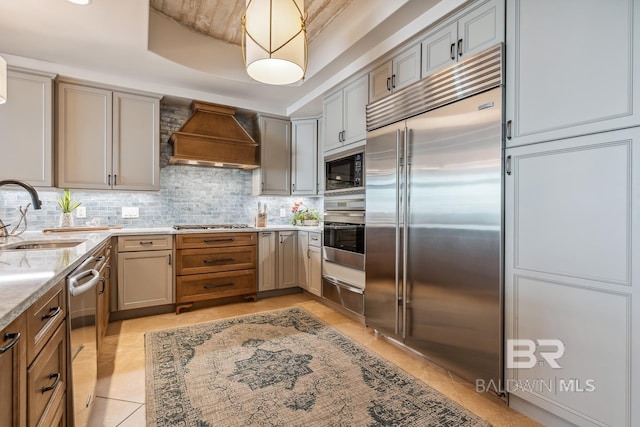 kitchen featuring custom range hood, a sink, a tray ceiling, tasteful backsplash, and built in appliances