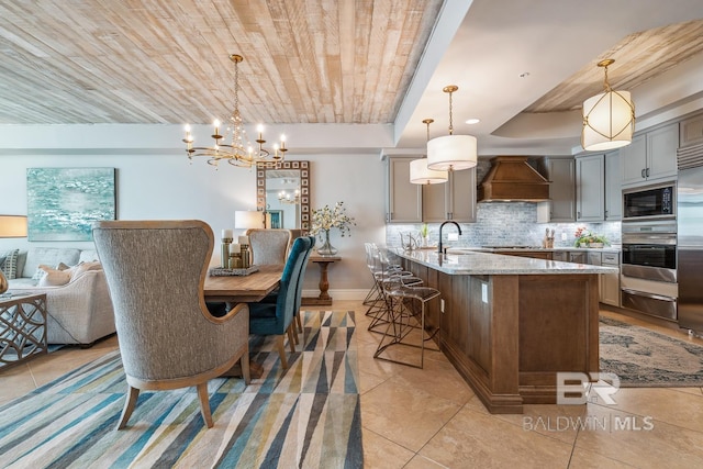 kitchen featuring custom range hood, built in appliances, a warming drawer, backsplash, and a chandelier