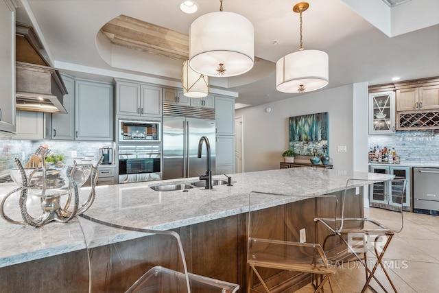 kitchen with tasteful backsplash, wine cooler, built in appliances, a kitchen breakfast bar, and a sink