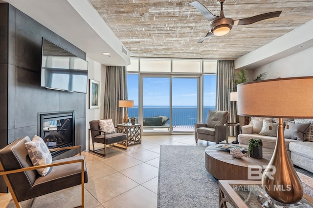 tiled living area with a wall of windows, visible vents, a glass covered fireplace, and a ceiling fan