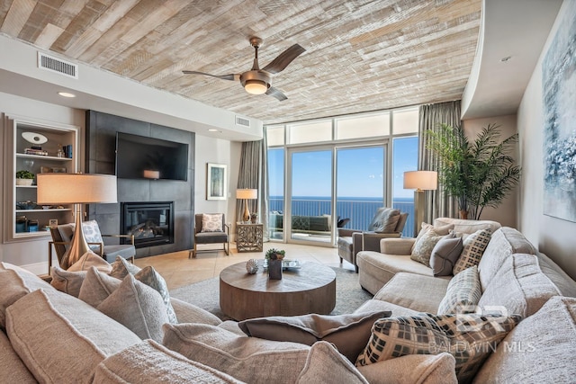 tiled living area with visible vents, ceiling fan, a tiled fireplace, wood ceiling, and a wall of windows