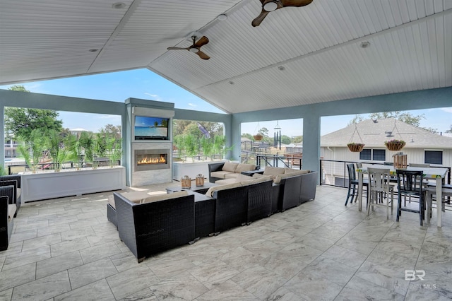 tiled living room featuring exterior fireplace, ceiling fan, and vaulted ceiling