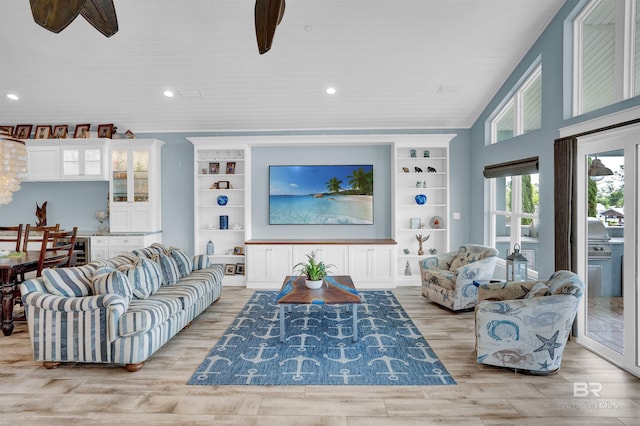 living room with built in shelves, light hardwood / wood-style floors, and ceiling fan