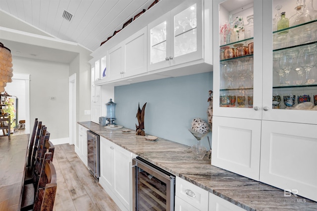 bar with white cabinets, lofted ceiling, light stone counters, and beverage cooler