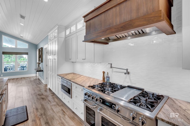 kitchen with stainless steel appliances, tasteful backsplash, custom exhaust hood, white cabinetry, and light wood-type flooring