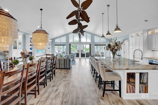 kitchen with light stone countertops, decorative light fixtures, light hardwood / wood-style flooring, white cabinetry, and a kitchen breakfast bar