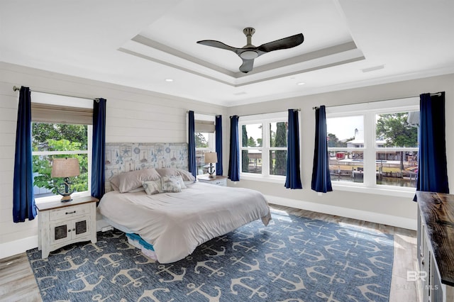 bedroom with hardwood / wood-style floors, ceiling fan, and a raised ceiling