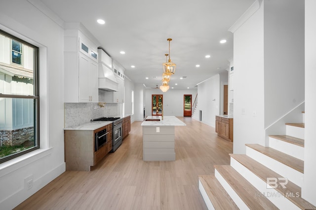 kitchen with hanging light fixtures, white cabinetry, high end stove, light hardwood / wood-style flooring, and a kitchen island with sink