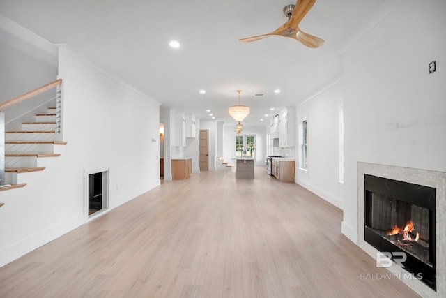 unfurnished living room featuring a tiled fireplace, light hardwood / wood-style floors, crown molding, and ceiling fan