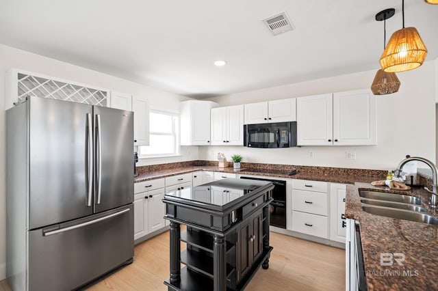 kitchen featuring black microwave, a sink, visible vents, white cabinetry, and freestanding refrigerator