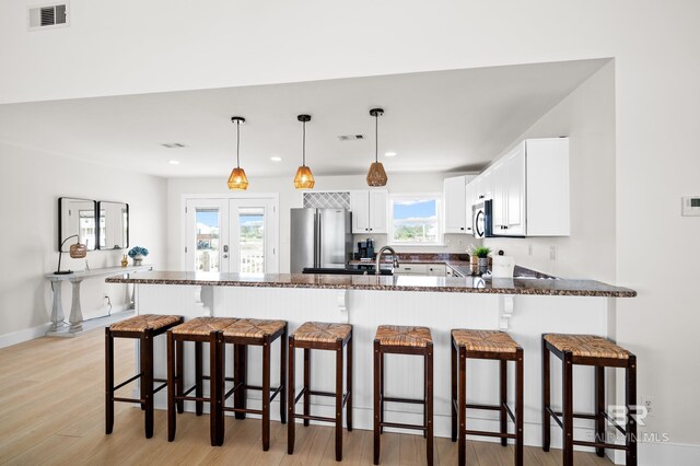 kitchen with stainless steel appliances, visible vents, white cabinetry, dark stone countertops, and a peninsula