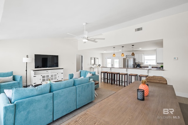 living area with lofted ceiling, visible vents, baseboards, a ceiling fan, and light wood finished floors