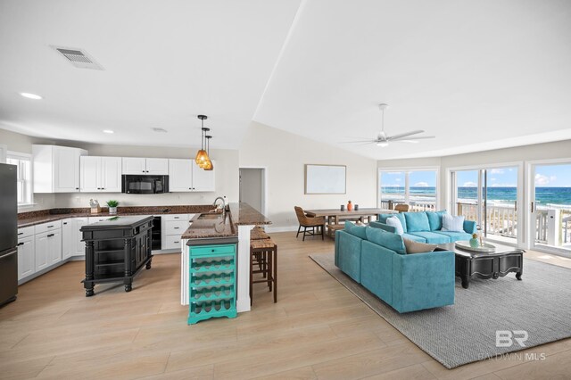 living room featuring vaulted ceiling, light wood-type flooring, visible vents, and a ceiling fan