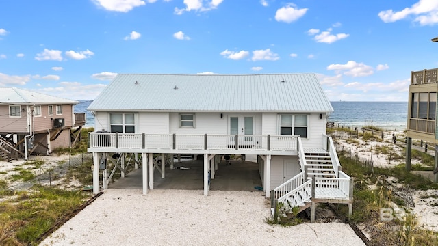 back of property featuring driveway, a water view, stairs, french doors, and a carport