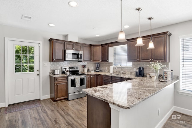 kitchen with kitchen peninsula, appliances with stainless steel finishes, a healthy amount of sunlight, sink, and hanging light fixtures