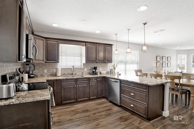 kitchen featuring kitchen peninsula, sink, appliances with stainless steel finishes, decorative light fixtures, and dark brown cabinets