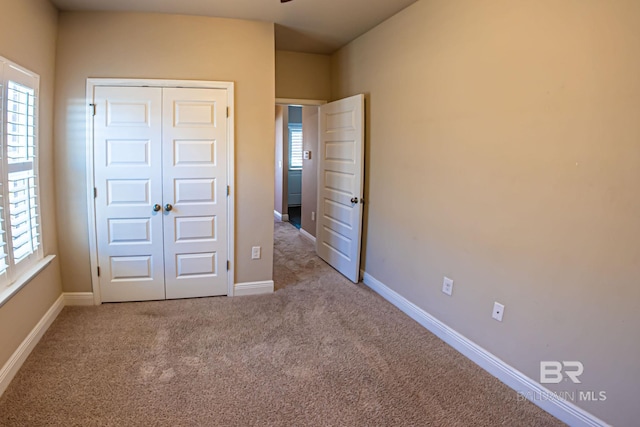 unfurnished bedroom with light carpet, multiple windows, a closet, and baseboards