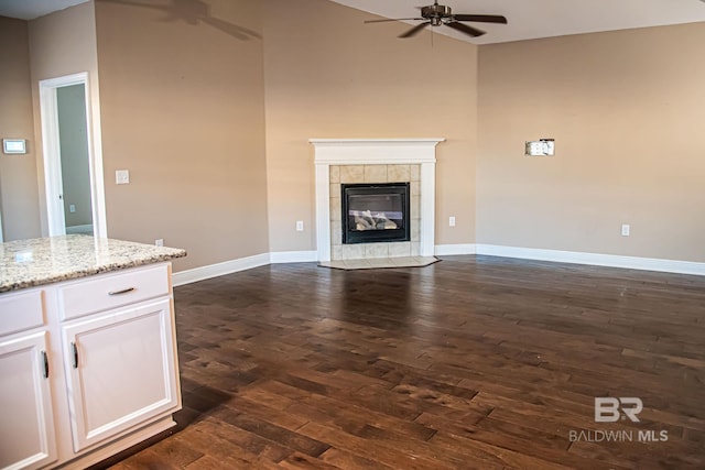 unfurnished living room with dark wood-style floors, baseboards, a ceiling fan, and a tile fireplace