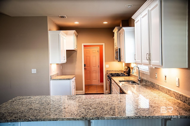 kitchen with light stone counters, stainless steel appliances, white cabinets, a sink, and a peninsula