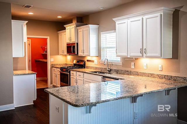 kitchen featuring appliances with stainless steel finishes, a breakfast bar area, a peninsula, light stone countertops, and a sink