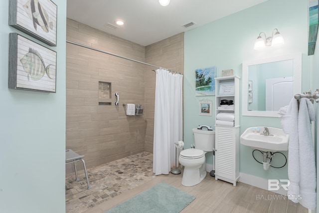 bathroom with a sink, visible vents, toilet, and a tile shower