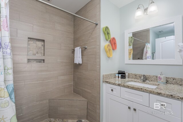 full bath featuring vanity, a tile shower, and visible vents