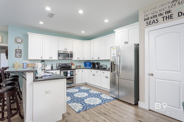 kitchen with white cabinetry, light wood-type flooring, stainless steel appliances, visible vents, and a peninsula