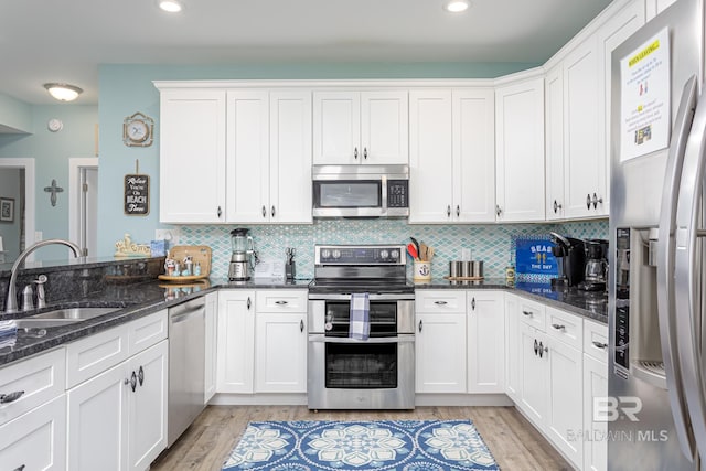 kitchen featuring a sink, white cabinetry, tasteful backsplash, stainless steel appliances, and light wood-style floors