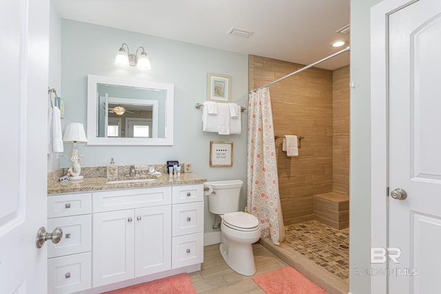 bathroom featuring toilet, tiled shower, vanity, visible vents, and ceiling fan