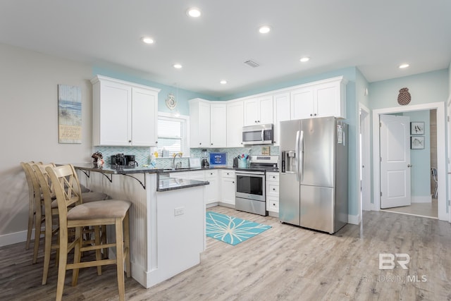 kitchen featuring stainless steel appliances, backsplash, a sink, light wood-style floors, and a peninsula