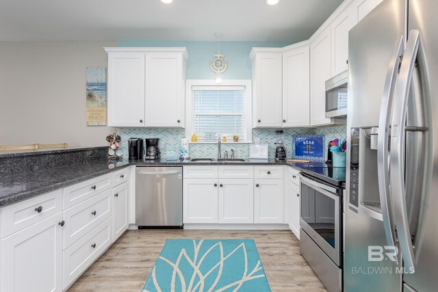 kitchen featuring a sink, appliances with stainless steel finishes, light wood-type flooring, white cabinets, and decorative backsplash