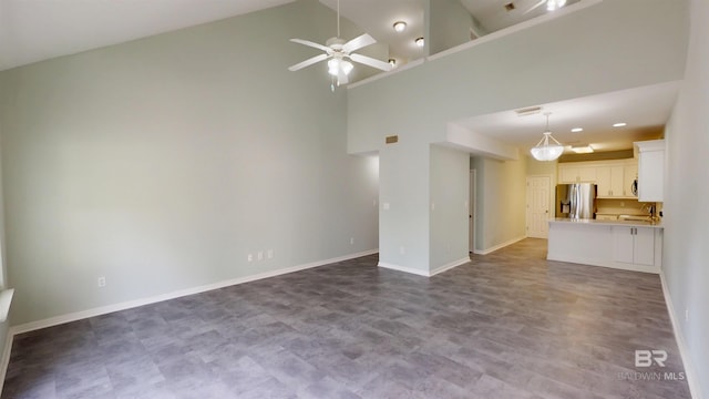unfurnished living room with baseboards, a sink, ceiling fan, and high vaulted ceiling