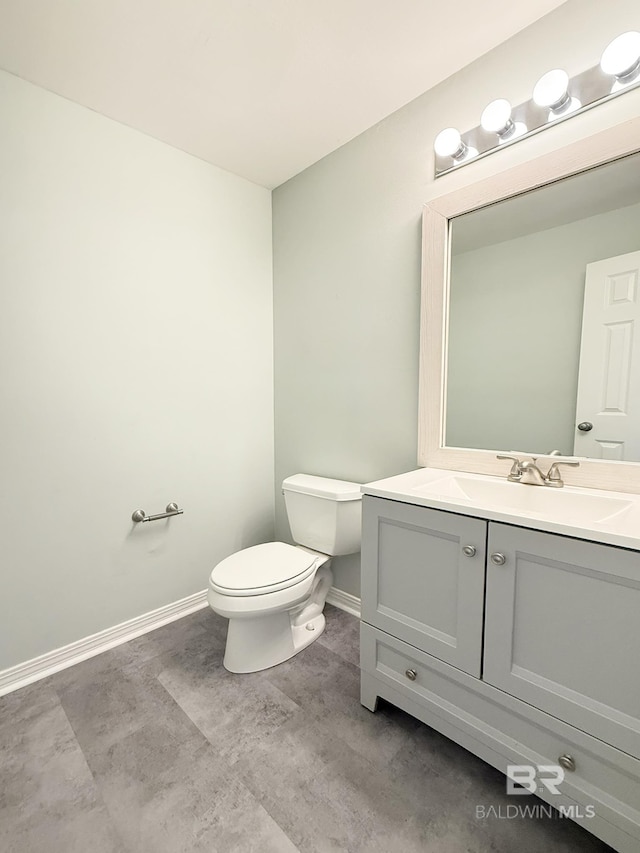 half bath featuring baseboards, vanity, and toilet