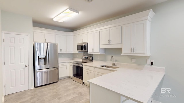 kitchen with white cabinets, a sink, light countertops, stainless steel appliances, and a peninsula