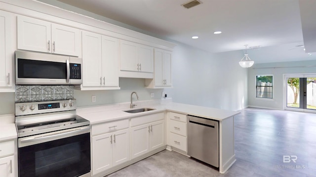 kitchen with a peninsula, light countertops, white cabinetry, a sink, and stainless steel appliances