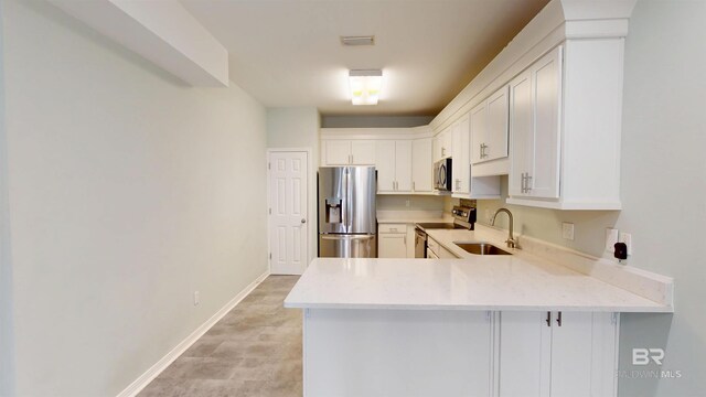kitchen with a sink, appliances with stainless steel finishes, white cabinets, and a peninsula