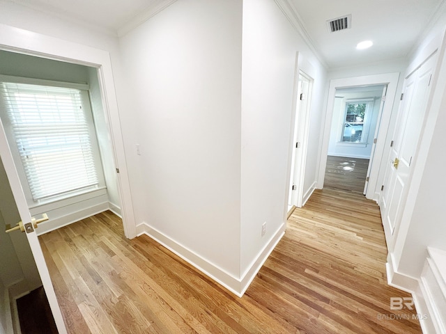 hallway with light wood-type flooring, baseboards, visible vents, and ornamental molding