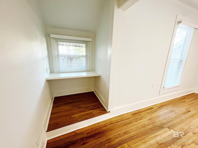 unfurnished room with built in study area, baseboards, and wood finished floors