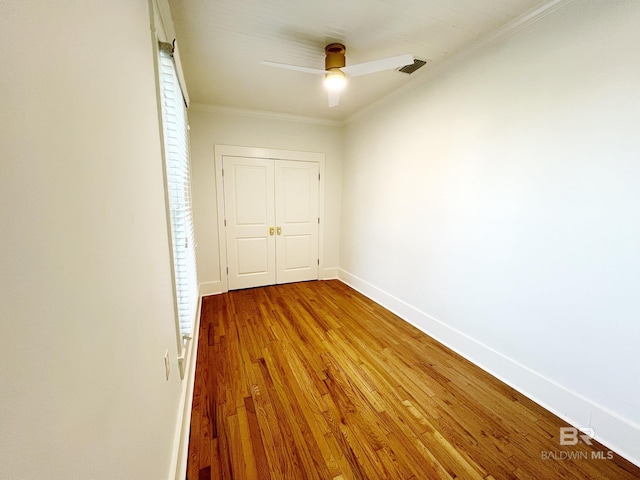 empty room with wood finished floors, visible vents, crown molding, baseboards, and ceiling fan