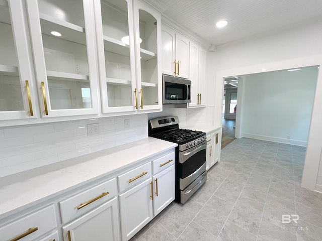 kitchen featuring decorative backsplash, appliances with stainless steel finishes, white cabinetry, and glass insert cabinets
