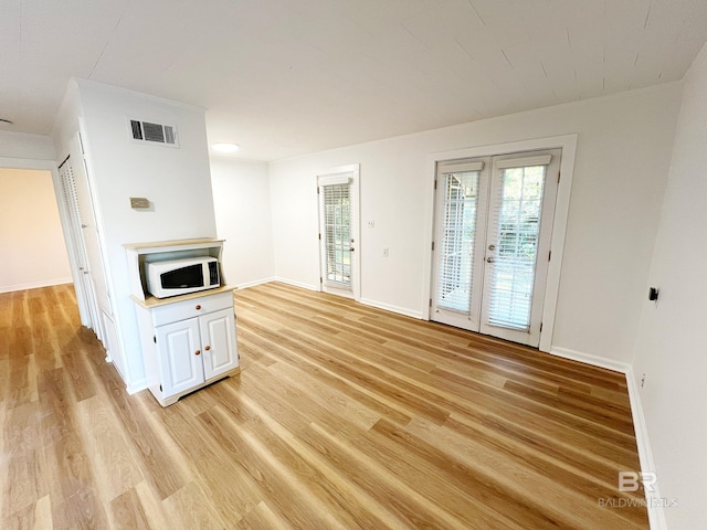 unfurnished living room with baseboards, french doors, light wood-style floors, and visible vents