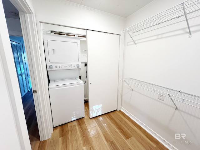 washroom with light wood-style floors, stacked washing maching and dryer, crown molding, and laundry area