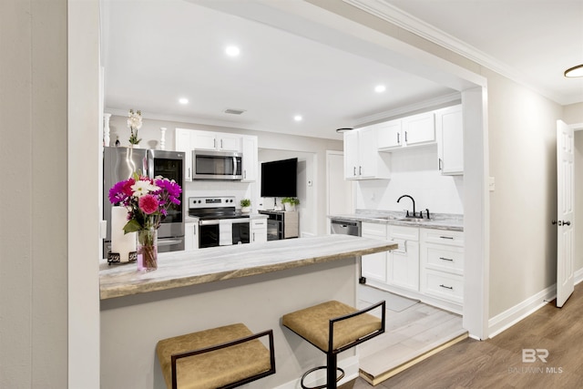 1508 Phillips Ln, Mobile, AL 36618 - kitchen with stainless steel appliances, a sink, crown molding, white cabinetry, and light wood-type flooring