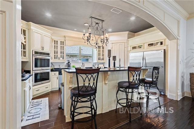 kitchen with pendant lighting, stainless steel appliances, dark wood-type flooring, and a center island with sink