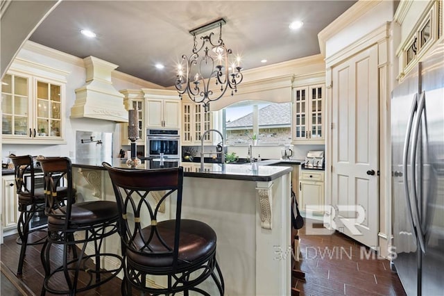 kitchen with stainless steel appliances, an island with sink, cream cabinetry, and decorative light fixtures