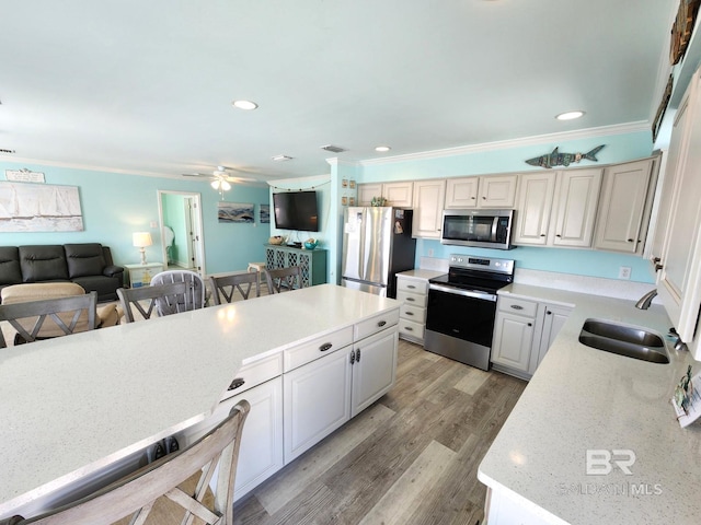 kitchen featuring light hardwood / wood-style flooring, appliances with stainless steel finishes, sink, white cabinets, and a kitchen bar